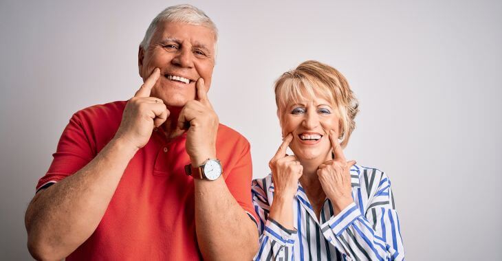 Smiling senior man and woman pointing at their teeth after clear choice dental implants treatment