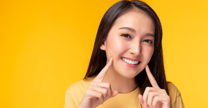 A smiling young woman pointing at her teeth.