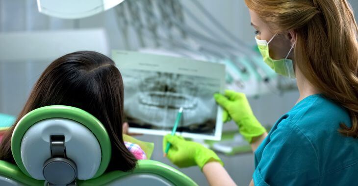 A periodontist discussing dental X-rays with the periodontal disease patient sitting in the dental chair.