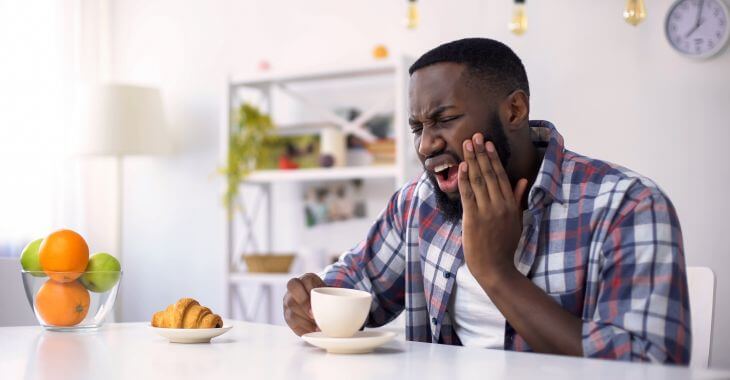 Afro-American man feeling severe tooth pain after having a sip of hot coffee.