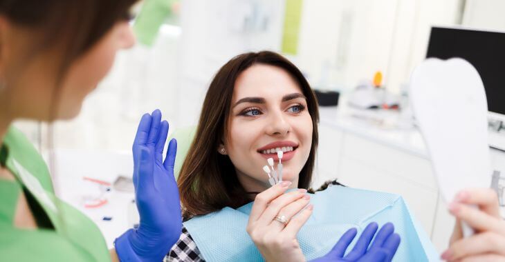 A cosmetic dentist helping young woman in a dental chair choose between veneers and Lumineers.