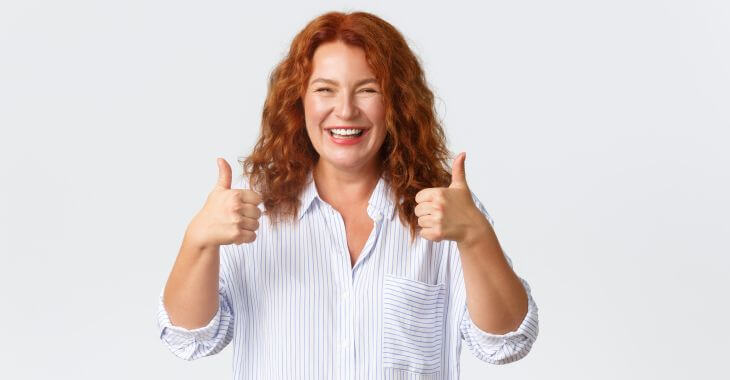 A happy woman after dental implant procedure showing her thumbs up.