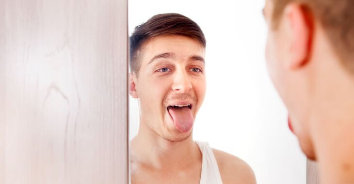 Young men sticking out his tongue watching in in the mirror.