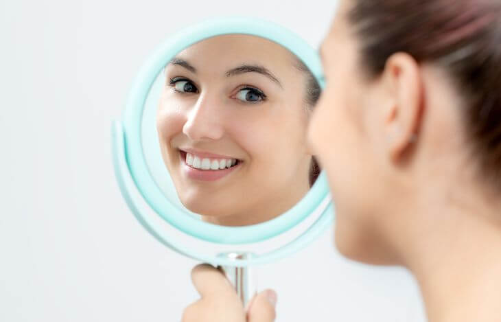 Girl looking at her teeth in a mirror.