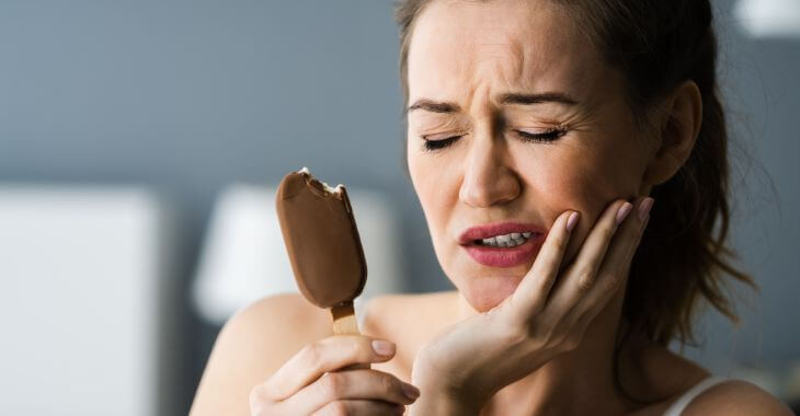 A woman with ice-cream suffering dental pain due to teeth sensitivity to cold. 