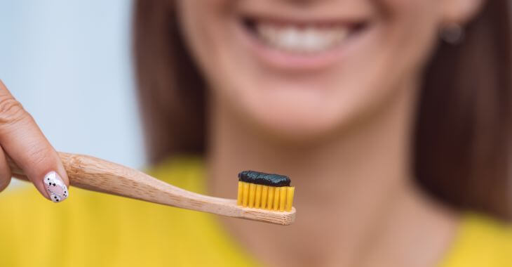 A young woman holding a toothbrush with charcoal toothpaste. 