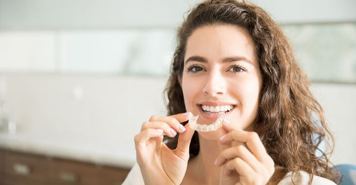 A woman with perfect teeth holding a dental retainer.