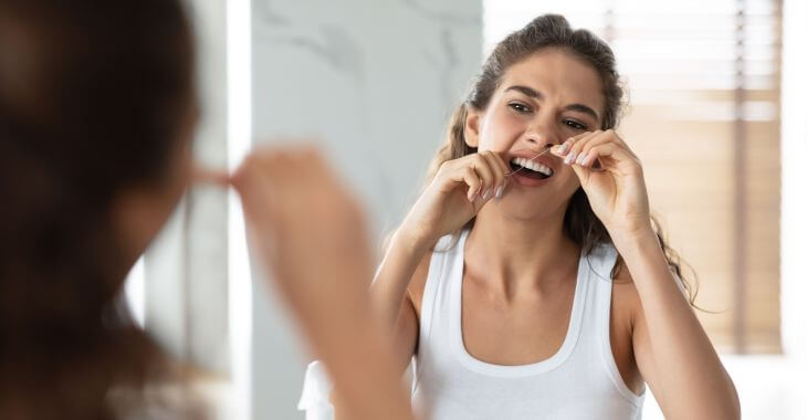 A young woman flossing her teeth.