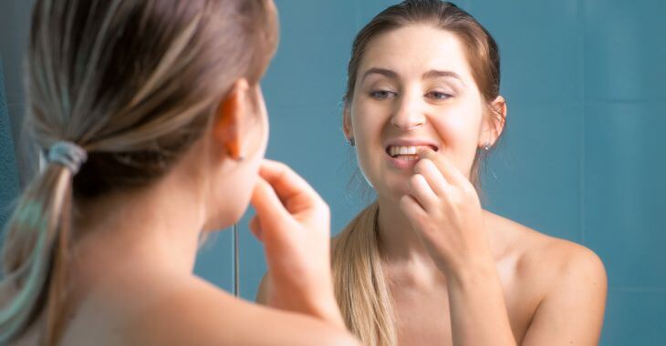 A woman  looking at her teeth and gums in the mirror.