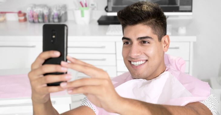 Happy young man in a dental chair taking selfie of his perfect smile.