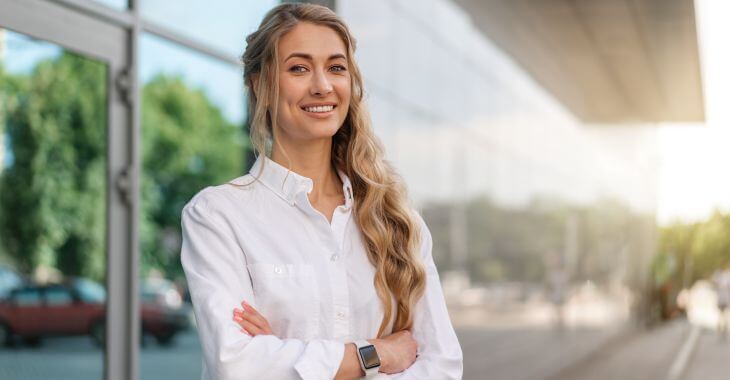 Confident young woman with perfect smile standing in front of an office building.