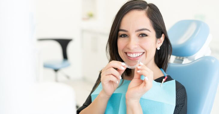 Happy young woman with perfect smile holding retainers during orthodontic appointment.