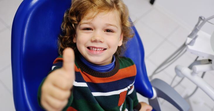 Smiling little boy in a dental chair showing his thumb up.