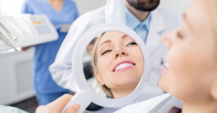 Woman in a dental chair looking at her perfect teeth in a mirror. 
