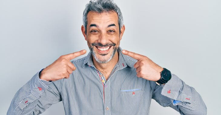 A happy broadly smiling middle-aged man pointing at his perfect teeth.