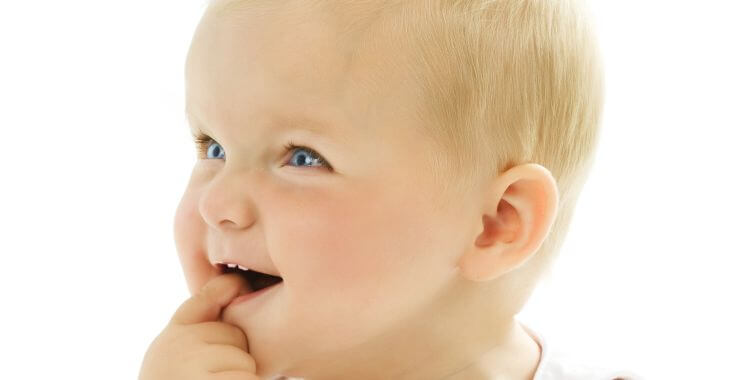 Smiling baby with two upper teeth putting a finger in their mouth.