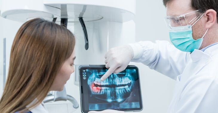 A patient and a dentist with a digital dental imaging pointing at teeth that need to be extracted.