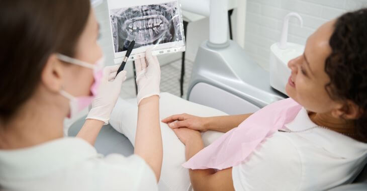 A dentist explaining dental x-ray to a woman sitting in a dental chair.
