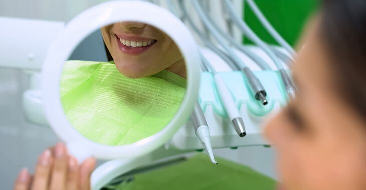 Woman in a dental chair holding a mirror and looking at her teeth after sealing procedure.