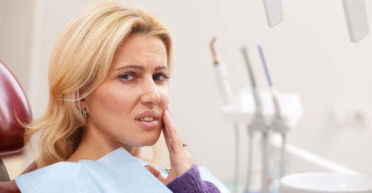 Concerned woman in a dental chair touching the area by her mouth.