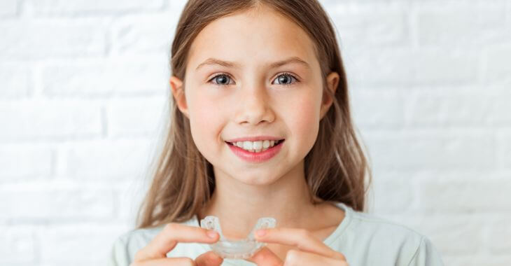 A girl with perfectly aligned teeth holding orthodontic aligner.