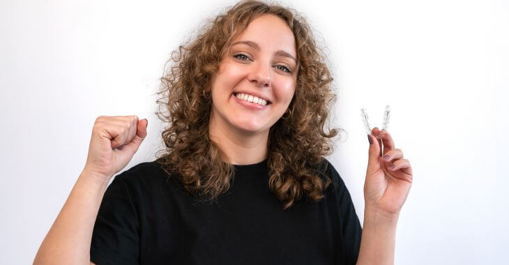 Happyyoung woman with a perfect smile holding a clear orthodontic aligner.