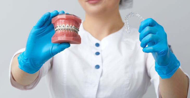 A dentist holding a dental model with traditional braces in one hand and a clear aligner in the other one.