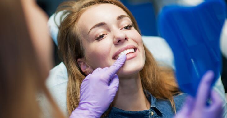 A woman during orthodontic appointment looking at her corrected smile in a mirror.