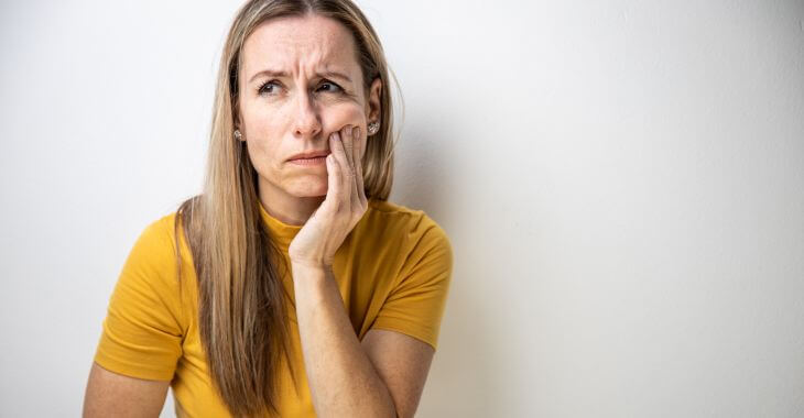 A concerned middle-aged woman touching her cheek due to dental issue.