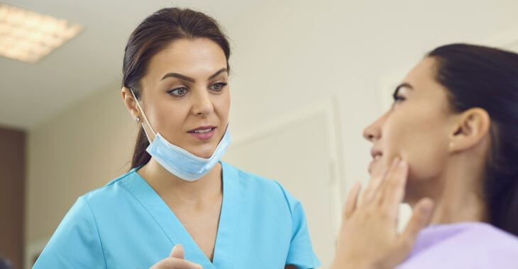 A dentist and a woman in a dental chair pointing at a painful tooth.