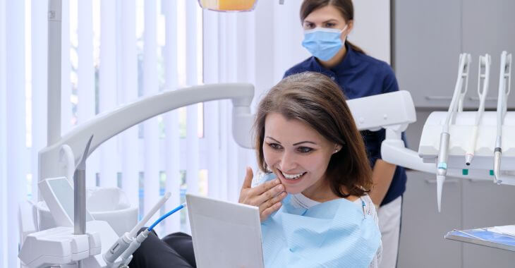 Happy woman after smile restoration looking at her teeth in a mirror.