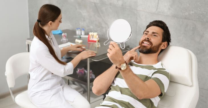 Satisfied man after dental implant restoration looking at his nice teeth in a mirror.