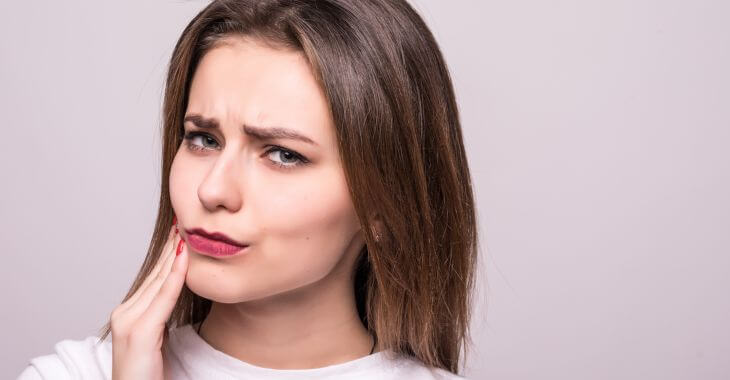 A concerned woman touching her cheek feeling a lump on her gum.