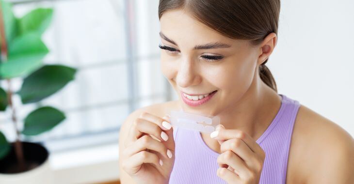 Young woman with a beautiful smile holding teeth whitening stripes.