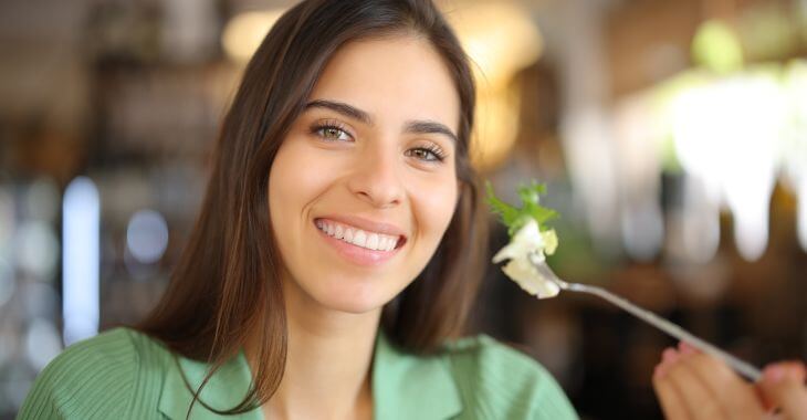 A happy smiling woman with white teeth eating a salad at a restaurant.