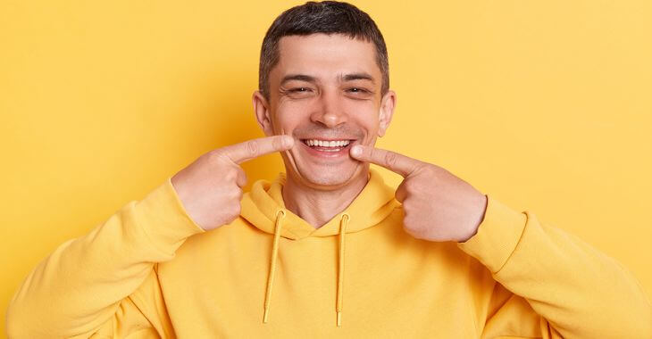 A happy middle-aged man pointing at his nice white teeth.