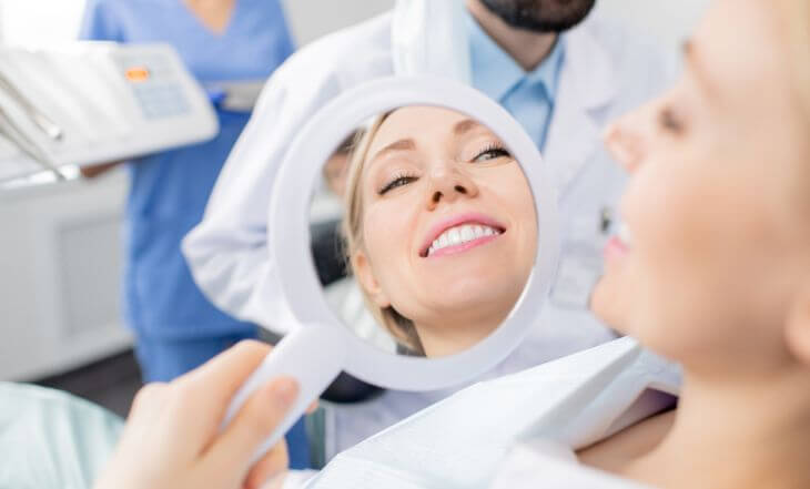 A happy dental patient after professional whitening looking at her teeth in a mirror. 