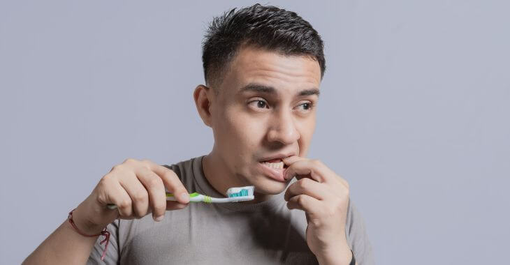 A concerned man with a toothbrush touching his gum as he feels a lump on in.