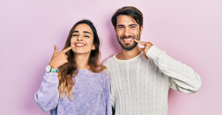 Young happily smiling woman and man pointing at their perfect teeth.