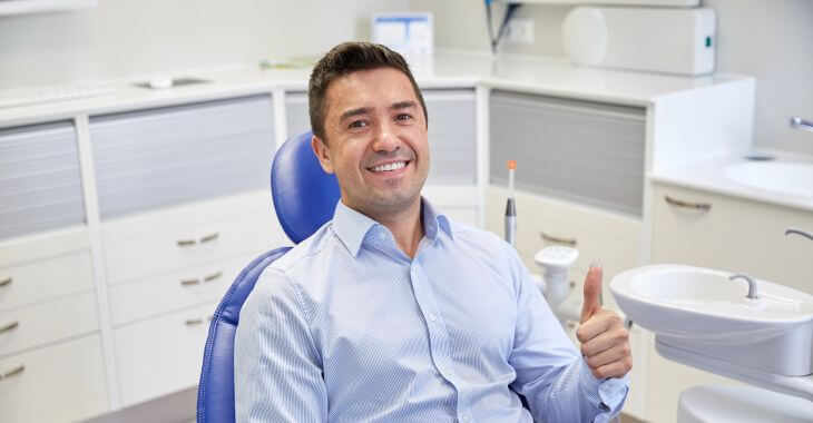 Satisfied cheerful middle0aged man in a dental chair showing his thumb up