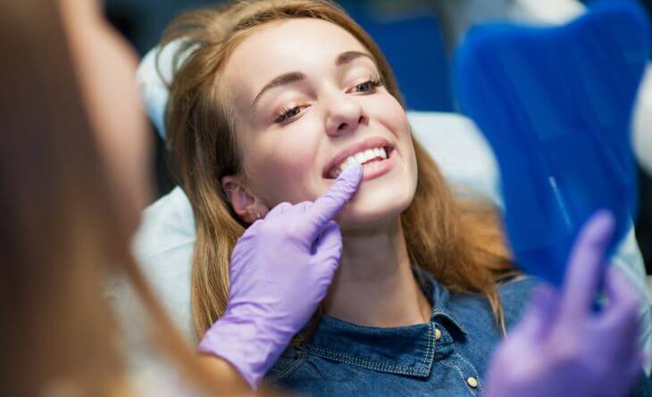 A dentist and a woman after dental crown placing looking at her teeth in a mirror. 
