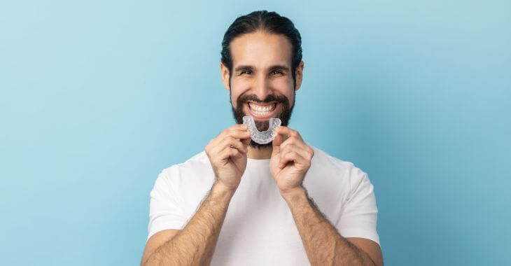 Happy middle-aged-man with a perfect smile holding an Invisalign retainer.