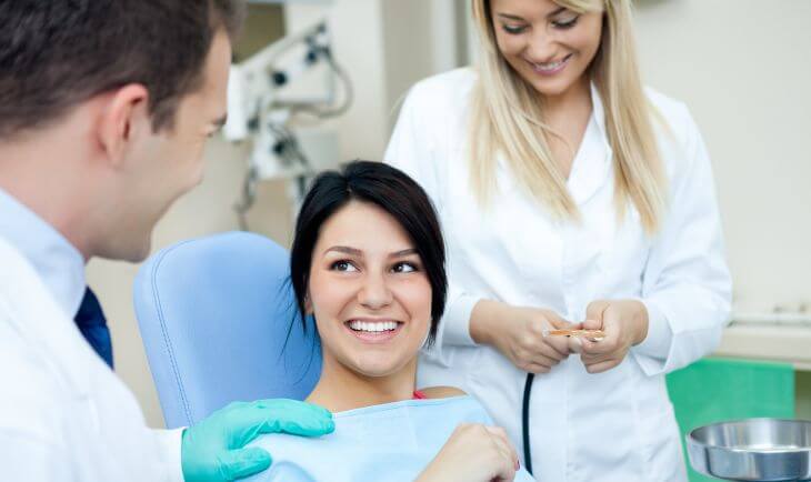 A satisfied woman in a dental chair discussing her treatment with a dentist. 