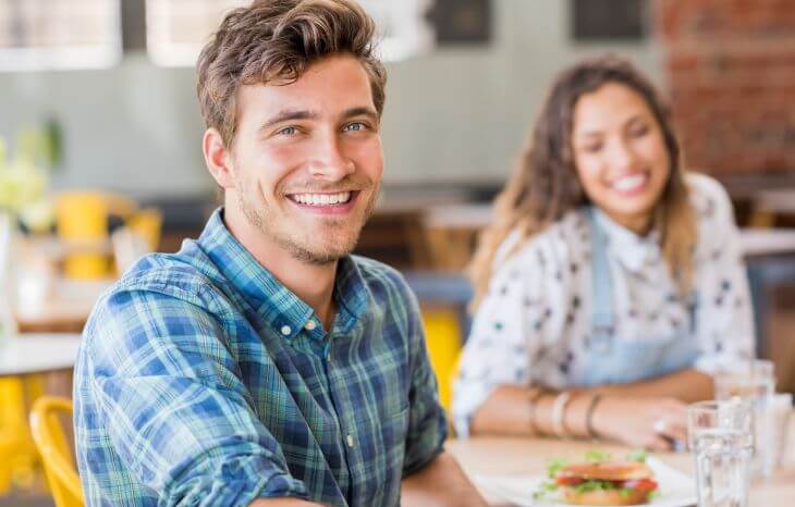 Happy smiling couple with perfect teeth sitting at the table with lunch sandwiches and beverages
