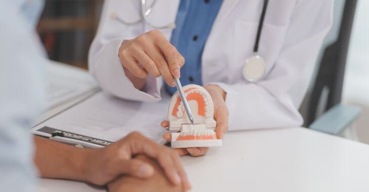 a patient and dentists explaining alveoloplasty on a dental model during dentures consultation