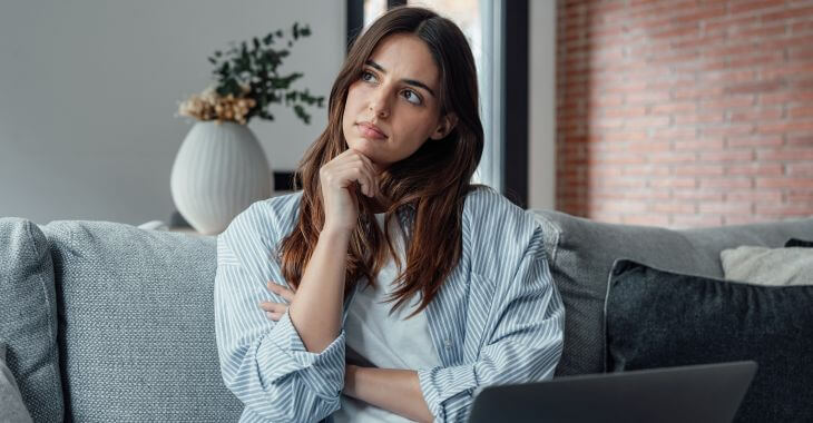 Thoughtful young woman sitting on the couch in front of a laptop