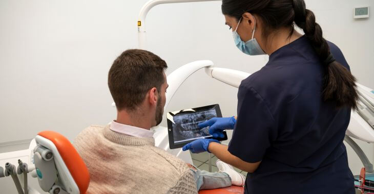 A dentist showing a digital dental x-ray image and explaining treatment options to a male patient sitting in a dental chair
