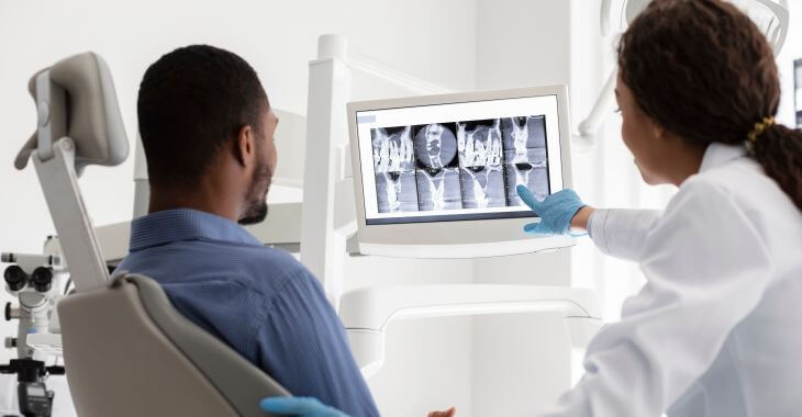 A dentist showing digital images to a male patient sitting in a dental chair