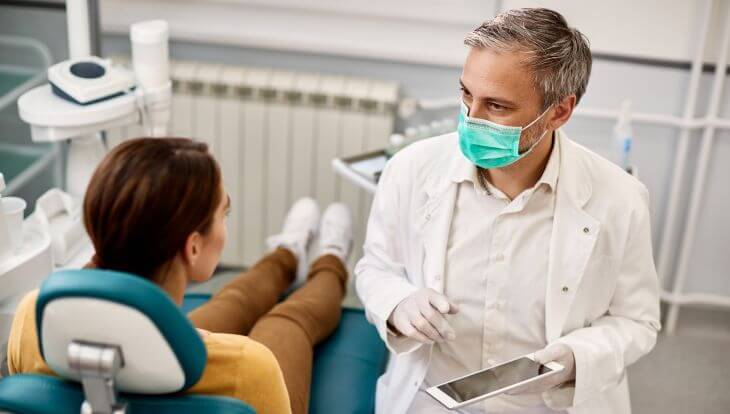 A dentist wit a tablet discussing treatment plan with a female patient sitting in a dental chair