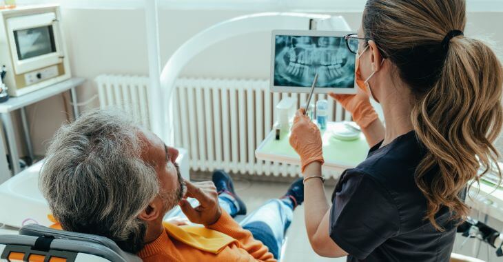 A concerned mature man in a dental chair listening to a dentist discussing his dental X-rays